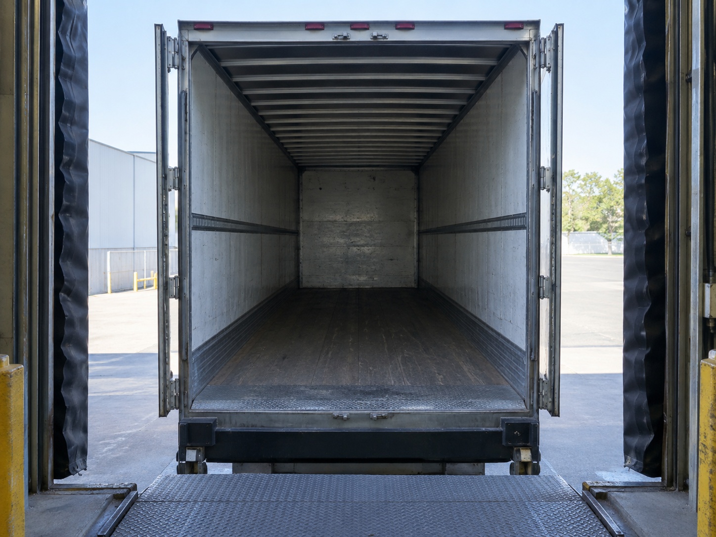 Looking straight into an empty trailer backed against a dock with its doors open, the floor bare from front to back and nobody working it.